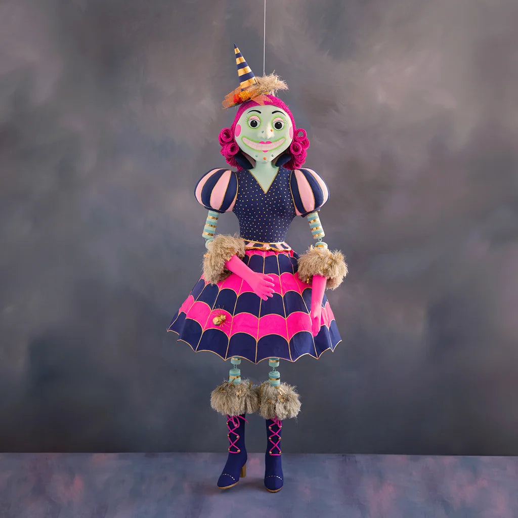 Glitterville Pinky Itchy Witchy large display doll featuring a green face, bright pink curled hair, striped navy and gold pointed witch hat, navy blue bodice with gold polka dots, pink and navy puff sleeves, striped turquoise arms, bright pink hands, and a full pink and navy spiderweb-patterned skirt with metallic gold detailing and a small spider embellishment. 