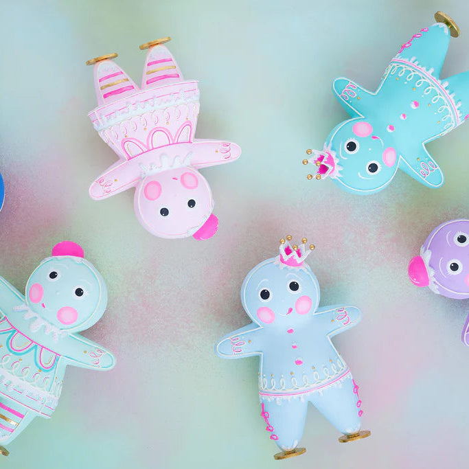 Close-up of Glitterville rainbow Dippsy and Dough gingerbread figures in soft pastel colors, featuring detailed pink and white icing, rosy cheeks, decorative buttons, gumdrop hats, crowns, gold accents, and whimsical holiday styling. The close-up showcases the intricate hand-iced details and colorful designs of these collectible Glitterville gingerbread Christmas figures.