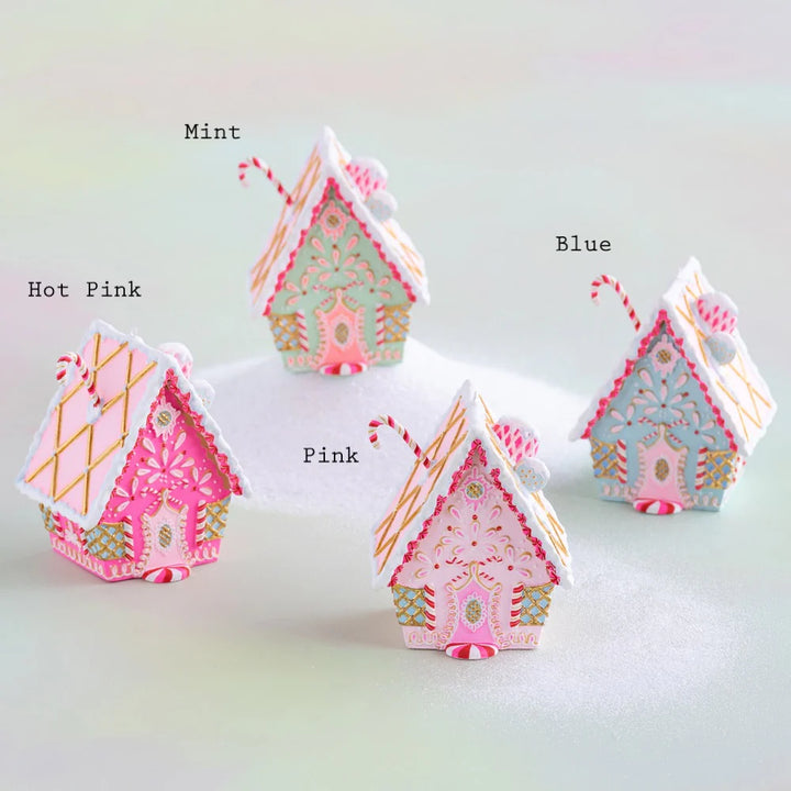 Glitterville rainbow gingerbread cottage Christmas ornaments displayed together and labeled by color as Mint, Hot Pink, Pink, and Blue. Each whimsical cottage ornament features intricate pink, white, and gold icing, candy-cane accents, peppermint details, gold lattice designs, snowy white roof trim, and colorful pastel gingerbread cottage designs for a playful holiday display.