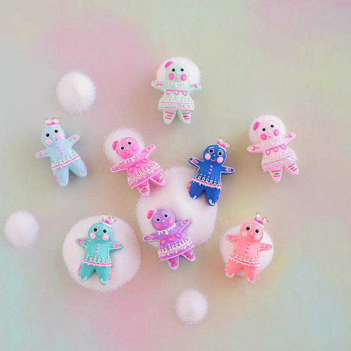 Rainbow multicolor Glitterville Dipsy and Dough gingerbread figure ornaments displayed on a soft pastel background, featuring blue, light blue, mint, teal, pink, hot pink, and violet figures with detailed white and pink icing, gold accents, and whimsical gumdrop headpieces.