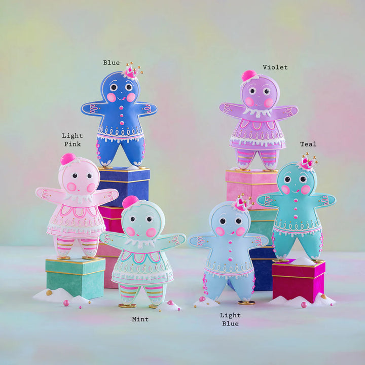 Glitterville Rainbow Dippsy &amp; Dough gingerbread figure collection featuring six colorful Christmas characters in Blue, Purple, Pink, Mint, Light Blue, and Teal, with each color labeled above its corresponding figure. The whimsical gingerbread figures feature detailed pink and white icing, rosy cheeks, decorative buttons, gumdrop hats and crowns, gold accents, and intricate hand-iced designs, displayed on colorful gift boxes in a soft pastel holiday setting.