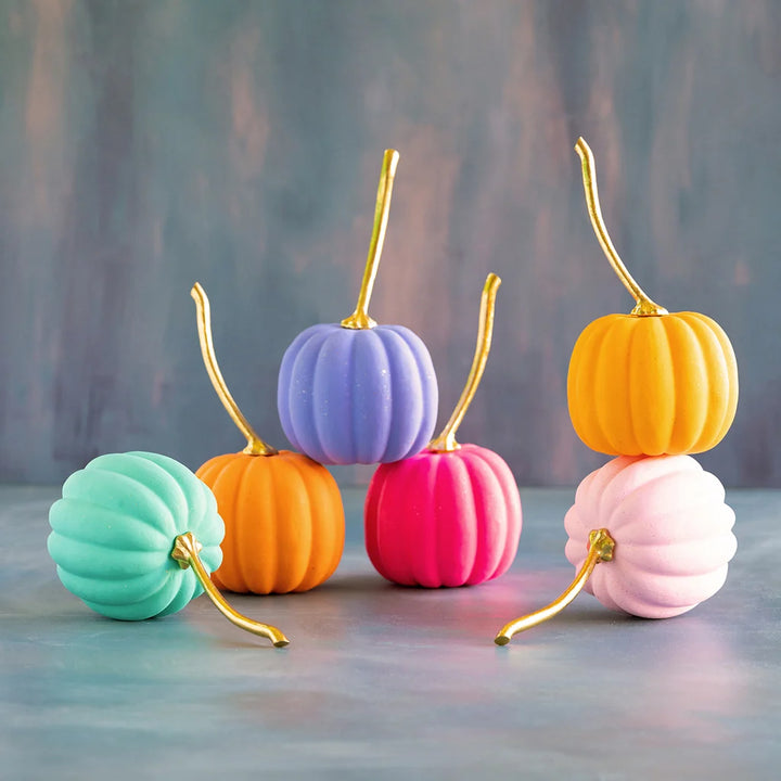Glitterville medium rainbow pumpkin set featuring five ribbed pumpkins in pastel mint, orange, lavender, hot pink, and pale pink, each finished with a long curved metallic gold stem. The pumpkins are arranged together on a softly colored tabletop against a blue and pink textured backdrop.