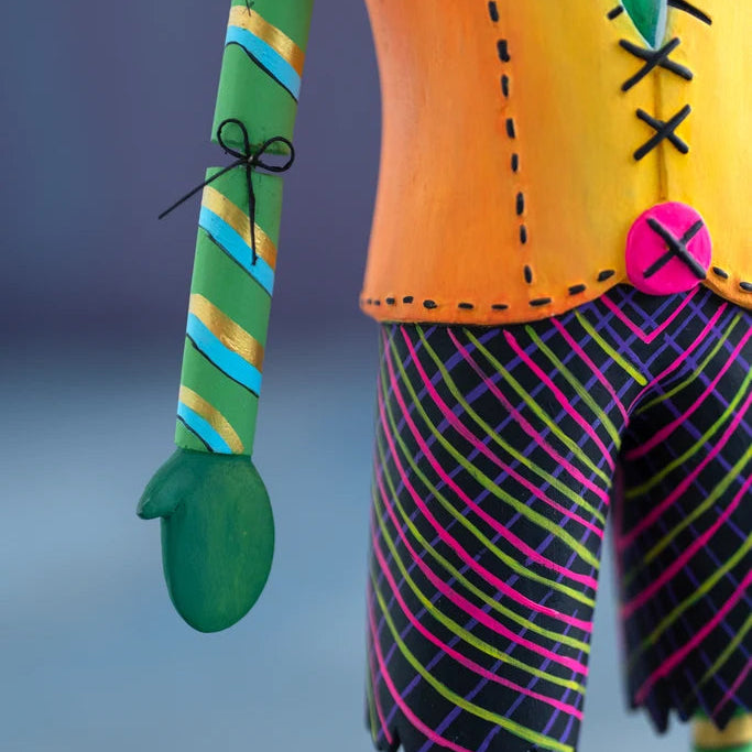 Close-up of the hand-painted Glitterville Swanky Franky Halloween ornament arm and waist, featuring a green striped arm with a black bow detail, bright orange stitched jacket, pink button, and colorful plaid pants.