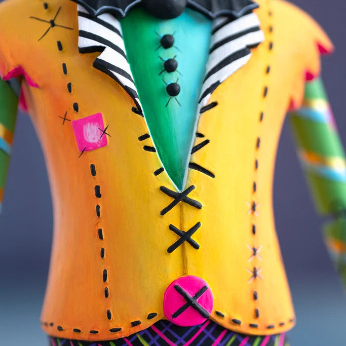 Close-up of the hand-painted Glitterville Swanky Franky Halloween ornament shirt, featuring a bright orange jacket with black stitched details, pink patches and buttons, a green center panel, and black-and-white striped collar.