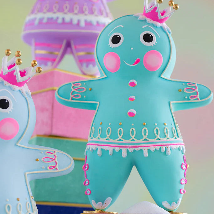 Close-up of the Glitterville Teal Dough gingerbread figure showcasing its vibrant teal color, pink and white icing details, gold accents, decorative pink buttons, looping white icing around the waist and arms, dripping white icing trim, rosy pink cheeks, and signature pink-and-gold crown. A detailed view highlighting the whimsical handcrafted-style design of this Glitterville gingerbread Christmas collectible.