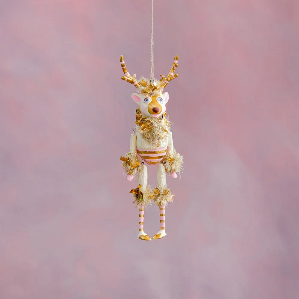 Gold and blush La Renne reindeer Christmas ornament with gold antlers, pink accents, striped body, and gold tinsel details hanging against a soft pink holiday backdrop.