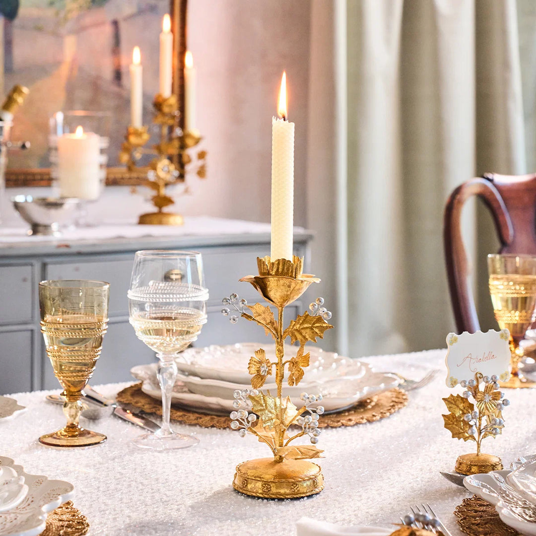 Gold Holly Taper Candle Holder with lit white candle styled on a festive table with gold glassware and holiday place settings