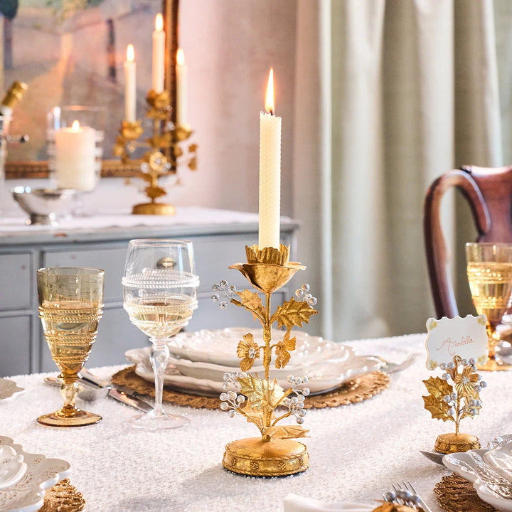 Gold Holly Taper Candle Holder with lit white candle styled on a festive table with gold glassware and holiday place settings