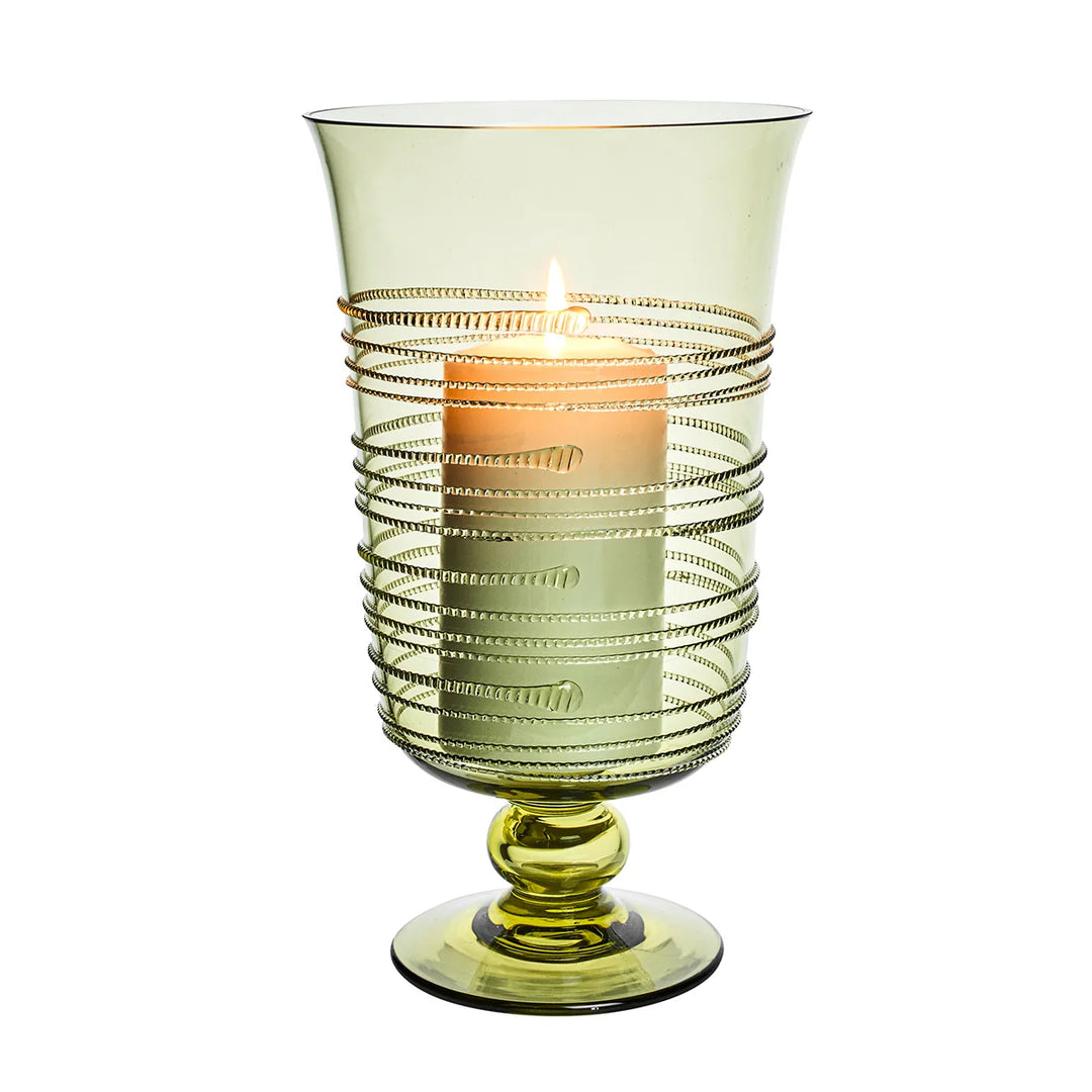 Green glass hurricane candle holder with decorative raised thread detailing and a glowing white pillar candle inside.