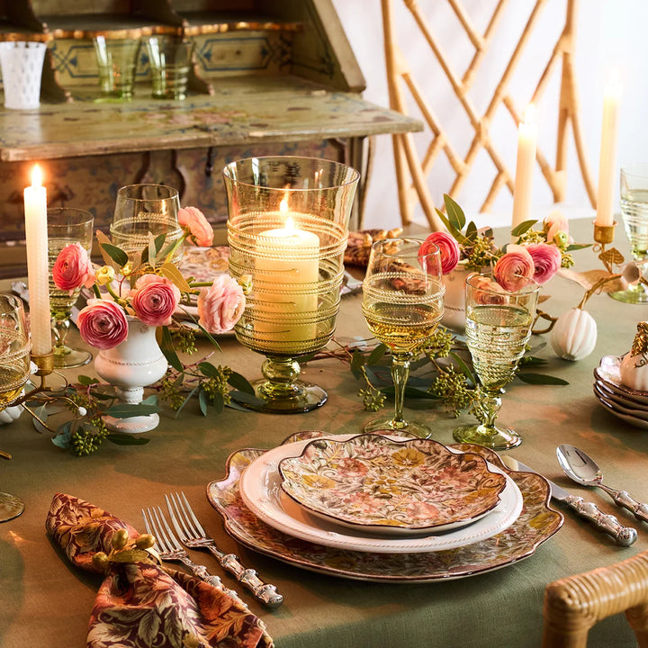 Green glass hurricane candle holder centerpiece styled with pink flowers, candles and coordinating green glassware on an elegant tablescape.