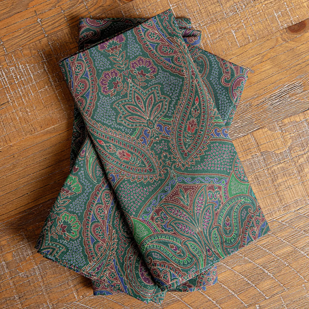 Forest green paisley cloth napkins featuring an intricate multicolor floral and scroll pattern displayed folded on a wood table.