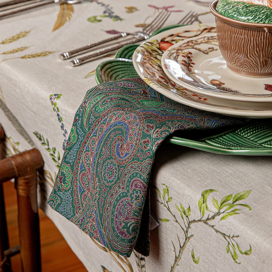 Green paisley cloth napkin draped beside layered botanical dinnerware for an elegant woodland-inspired table setting.
