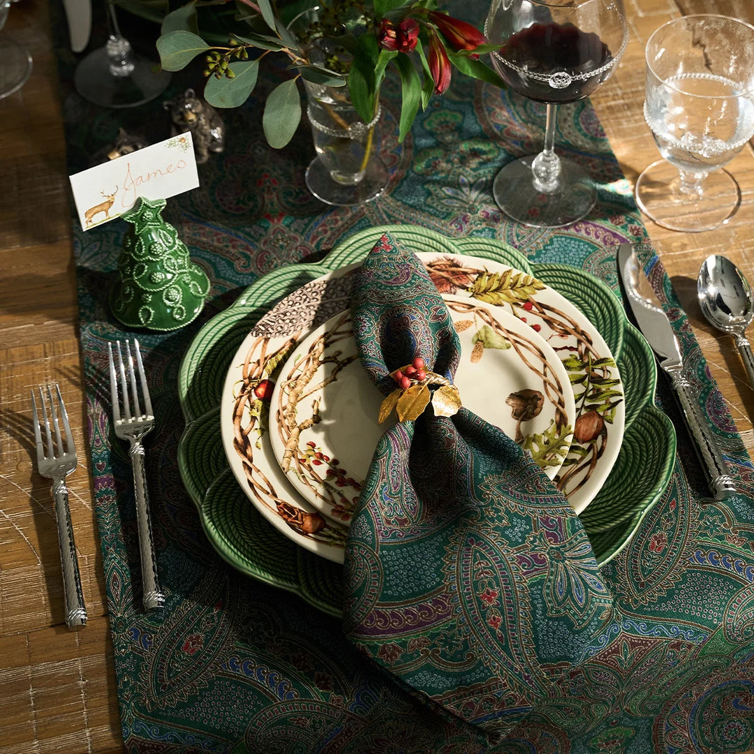 Green paisley cloth napkin styled on an elegant woodland tablescape with green dinnerware, botanical plates and holiday accents.
