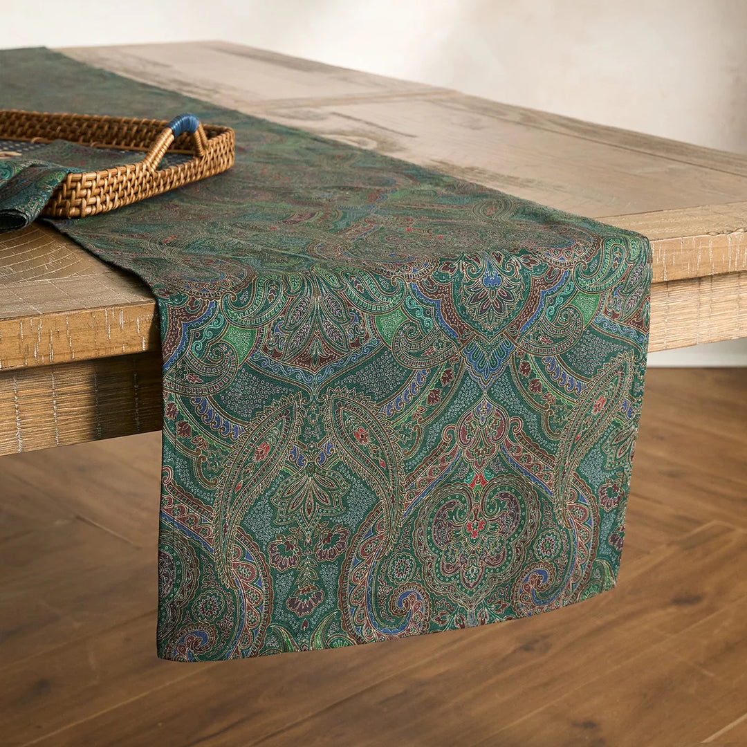 Green paisley table runner styled on a wood dining table with a woven tray, creating an elegant traditional tablescape.