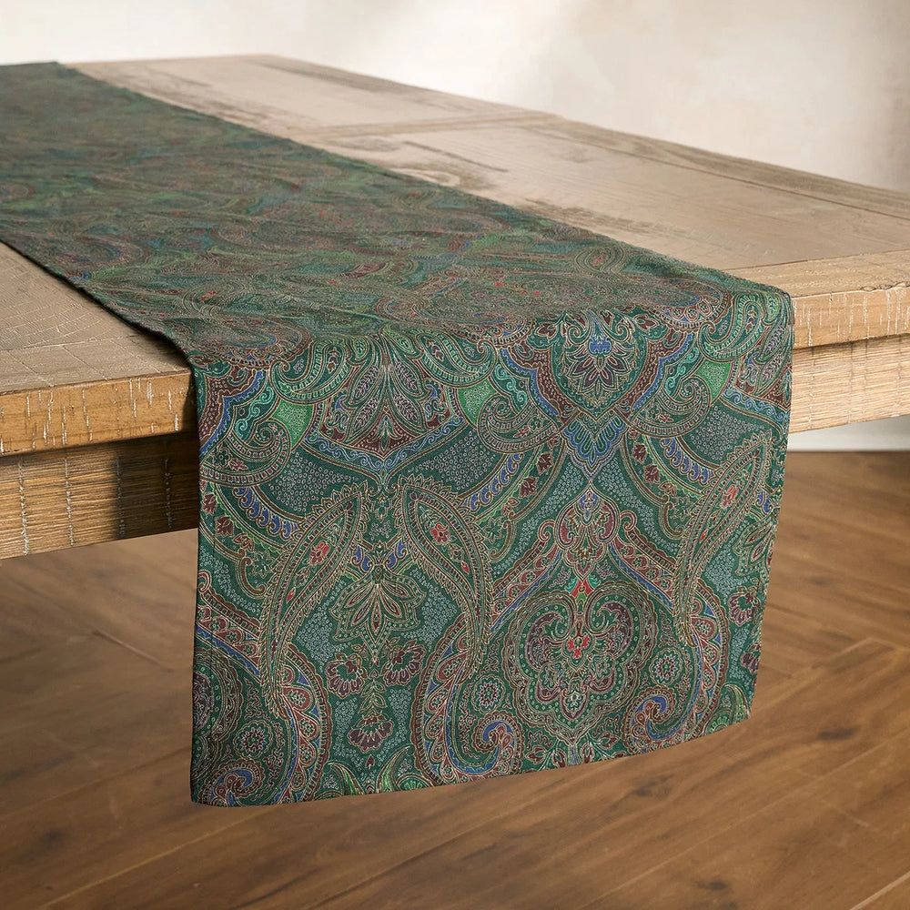 Green paisley table runner draped lengthwise across a natural wood dining table, showcasing its intricate multicolor paisley design.