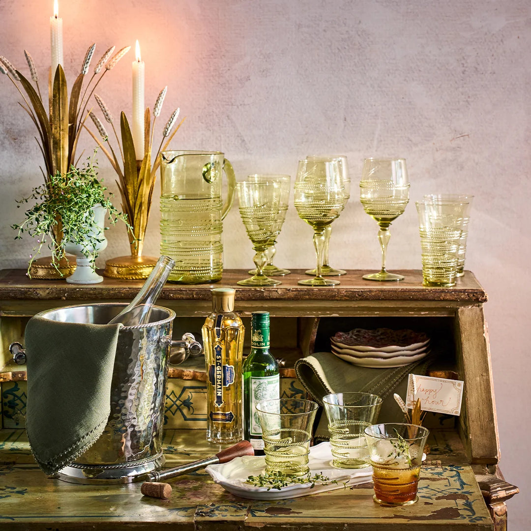 Juliska Amalia green footed goblets displayed with coordinating green glassware and pitcher in an elegant entertaining bar setting.