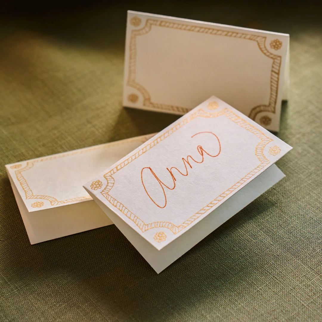 Juliska Berry &amp; Thread Place Cards styled on a green tablecloth, including a personalized folded place card with elegant gold detailing.