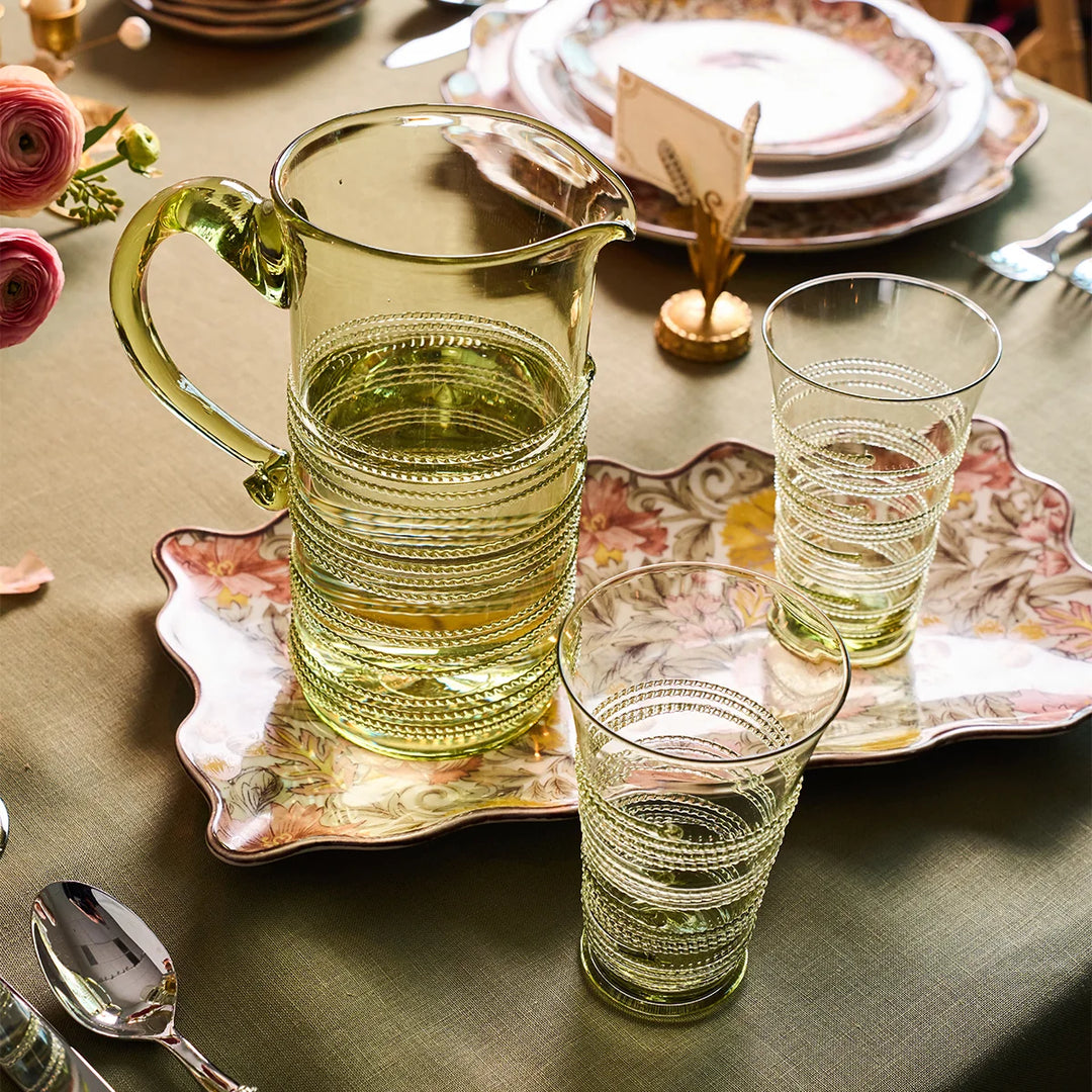 Juliska green glass highball tumblers with decorative wrapped thread detailing styled beside a coordinating pitcher on an elegant tablescape.