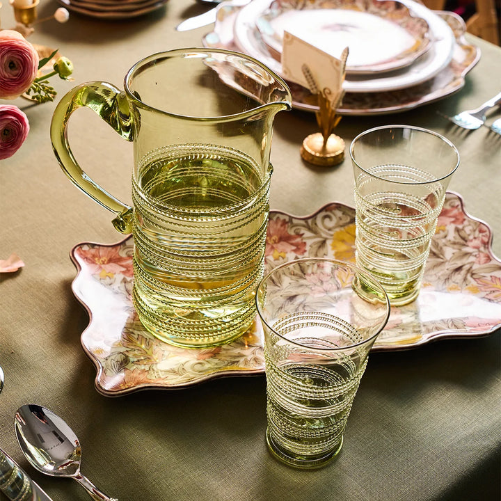 Juliska green glass highball tumblers with decorative wrapped thread detailing styled beside a coordinating pitcher on an elegant tablescape.
