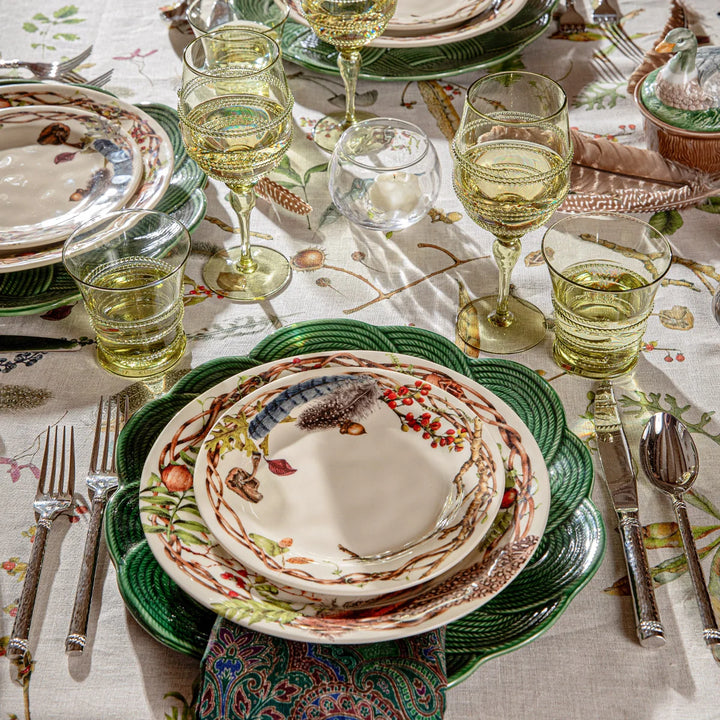 Juliska green glass tumblers and wine glasses arranged around an elegant botanical dinnerware place setting with green chargers.