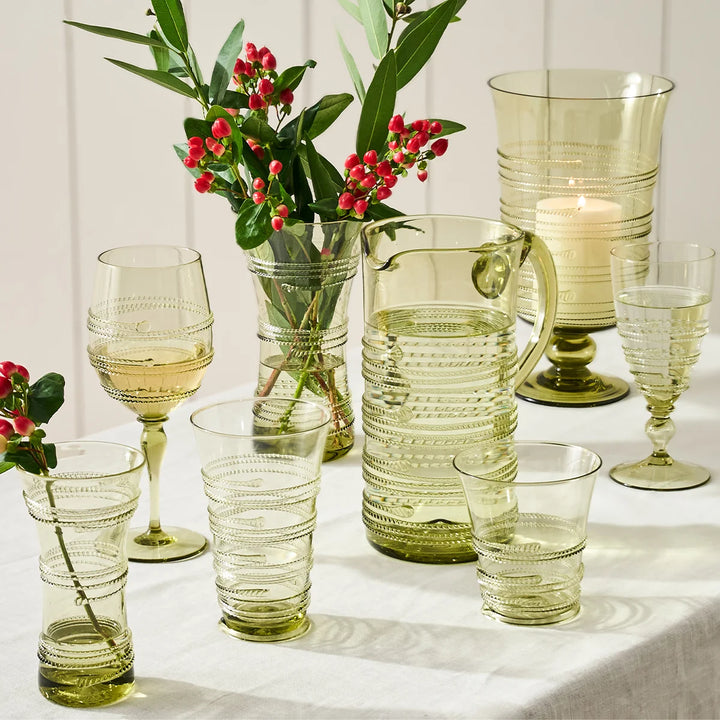 Juliska green glass vase styled with red berry branches among coordinating green glassware and a hurricane candle holder.