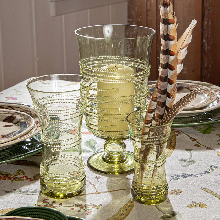 Juliska green glass vase displayed on an elegant woodland-inspired tablescape with coordinating green glass hurricane and decorative feathers.