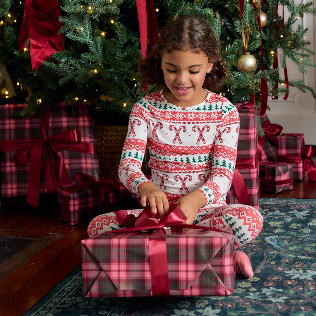 Girl wearing Candy Cane Fair Isle bamboo Christmas pajamas while opening a holiday gift beneath a decorated Christmas tree.