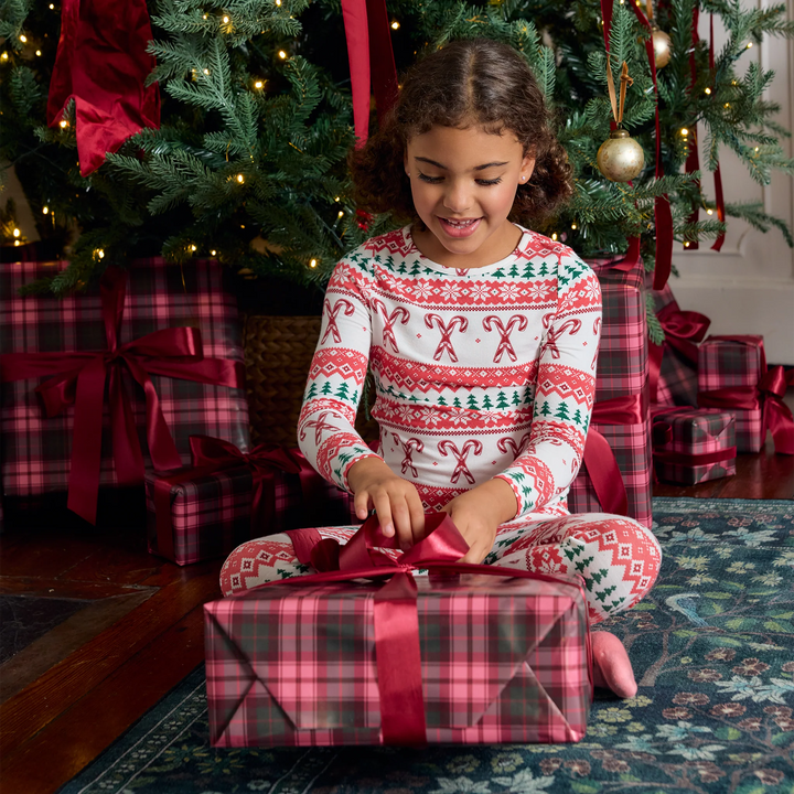 Girl wearing Candy Cane Fair Isle bamboo Christmas pajamas while opening a holiday gift beneath a decorated Christmas tree.