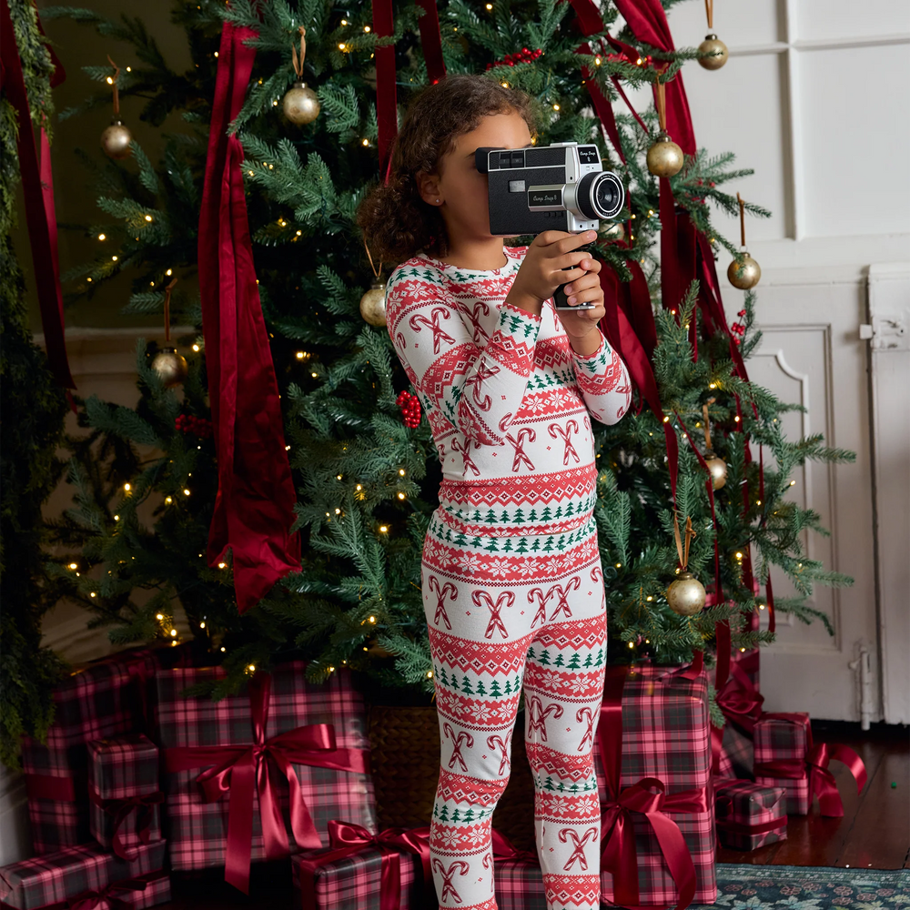 Child wearing Candy Cane Fair Isle bamboo Christmas pajamas while holding a vintage camera beside a decorated Christmas tree.