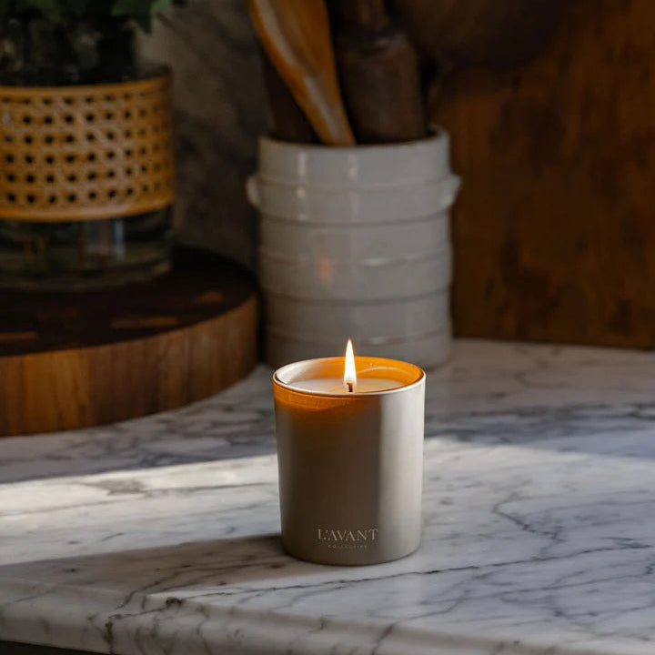 Lit L’AVANT Collective Ambre Santal candle styled on a marble countertop in a warm home interior.