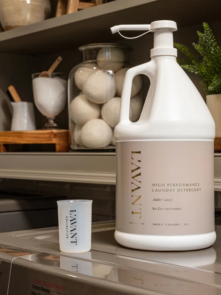 L’AVANT Collective Ambre Santal gallon laundry detergent with measuring cup in laundry room