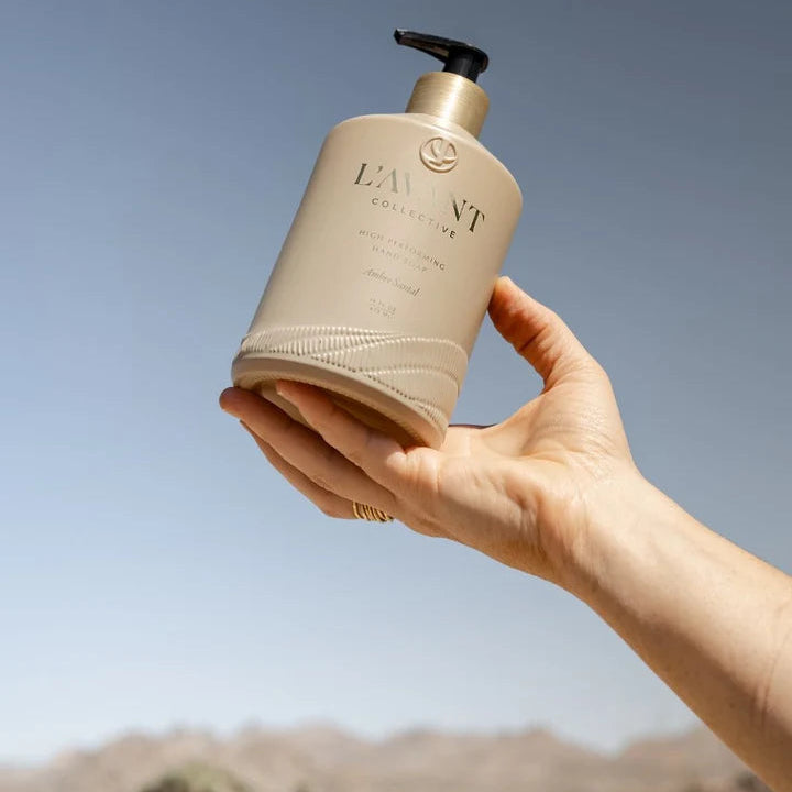 L’AVANT Ambre Santal High Performing Hand Soap 16 oz bottle held outdoors against a blue sky and desert landscape
