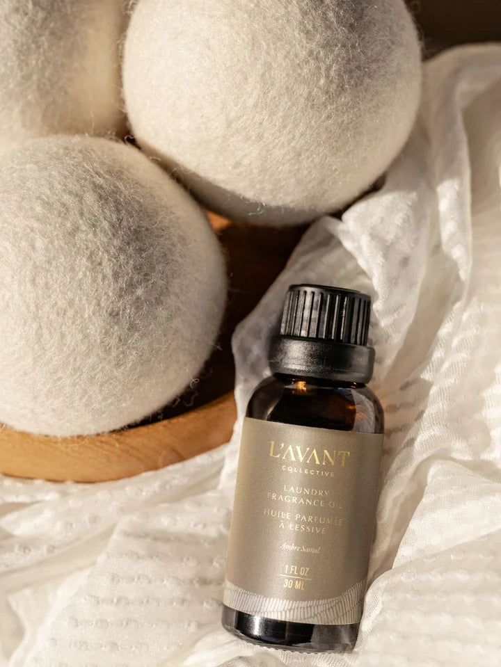L’AVANT Collective Ambre Santal Laundry Fragrance Oil styled with white wool dryer balls and soft textured linens.
