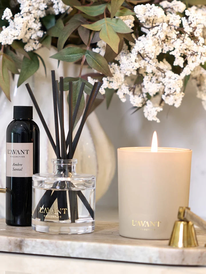 L’AVANT Collective Ambre Santal reed diffuser with refill oil and black reeds styled beside a candle and floral arrangement.
