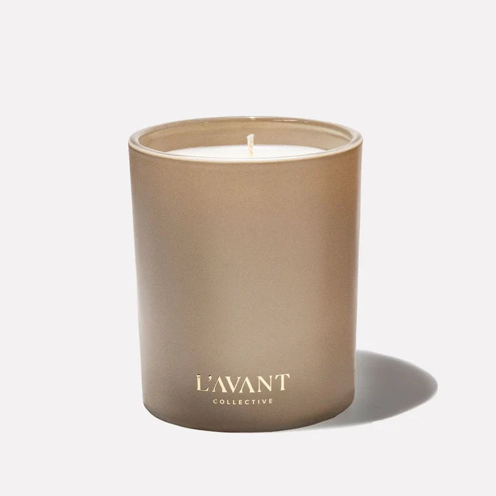 L’AVANT Collective Ambre Santal scented candle in a neutral taupe glass vessel with gold logo.