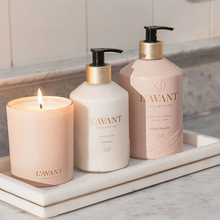 L’AVANT Collective Blushed Bergamot candle styled with hand lotion and hand soap on a marble vanity tray.