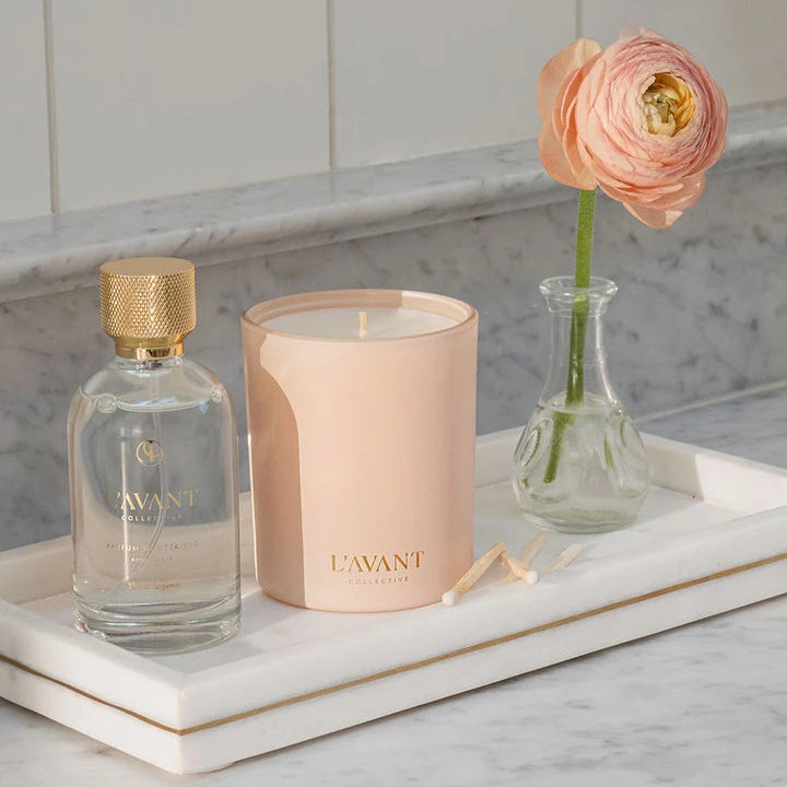 L’AVANT Collective Blushed Bergamot candle styled with room spray and a pink flower on a marble tray.