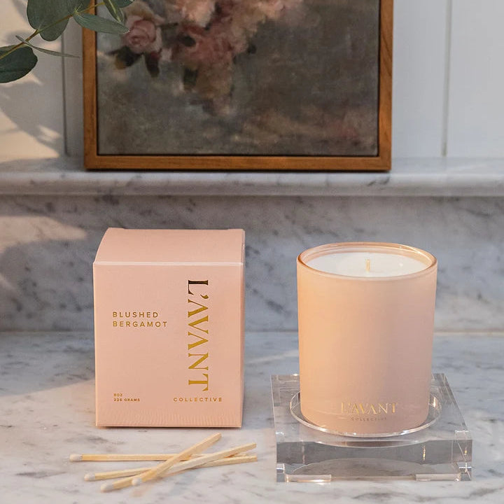 L’AVANT Collective Blushed Bergamot candle with pink product box and matches displayed on a marble countertop.
