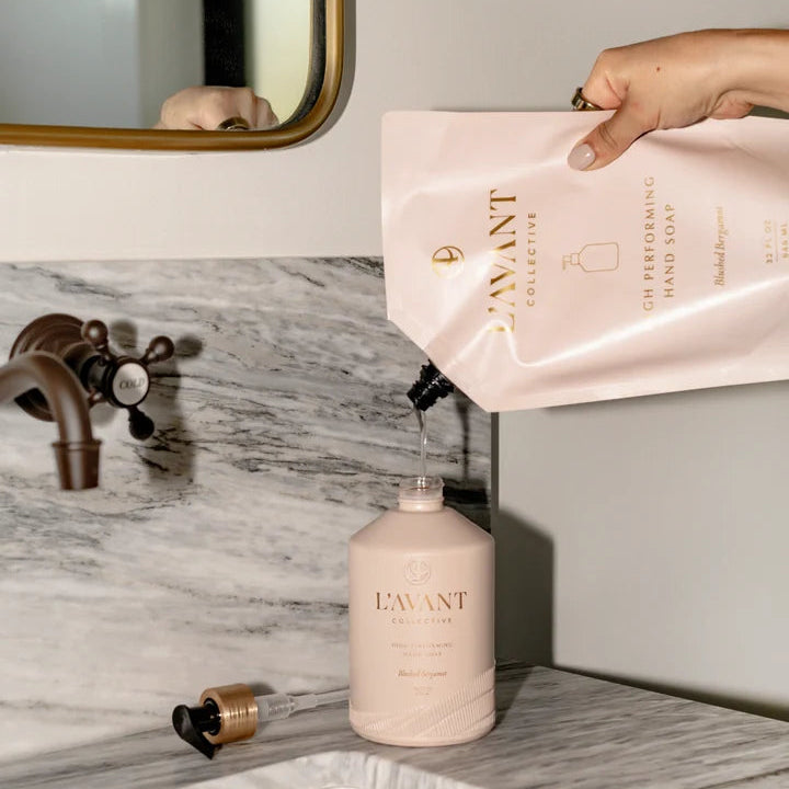 L’AVANT Blushed Bergamot hand soap refill pouch being poured into a reusable High Performing Hand Soap bottle