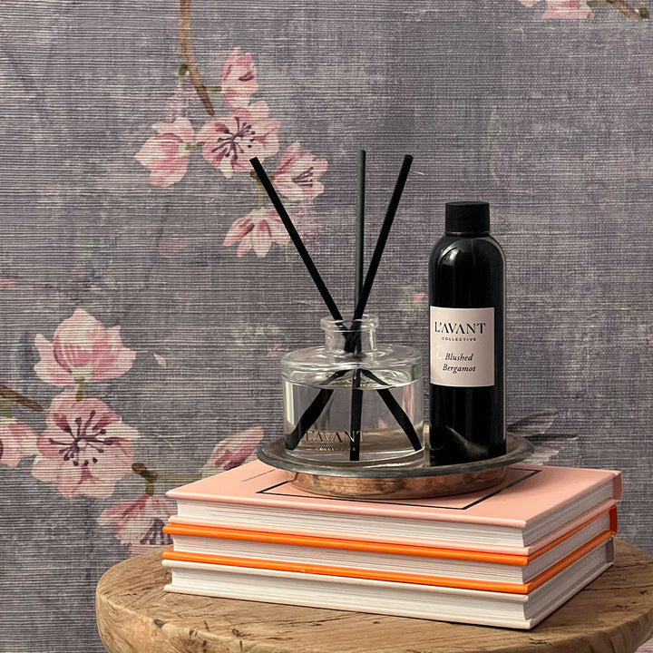 L’AVANT Collective Blushed Bergamot reed diffuser and refill oil styled on books against a floral background.
