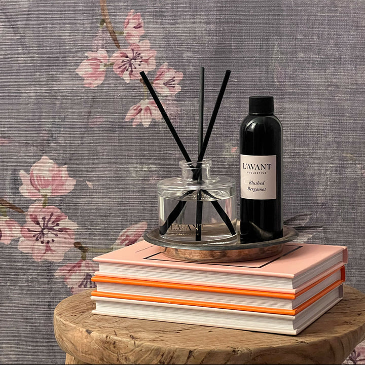 L’AVANT Collective Blushed Bergamot reed diffuser with black reeds and matching fragrance refill styled on books against a floral backdrop.