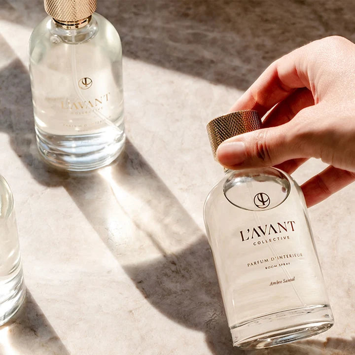 L’AVANT Collective Ambre Santal Parfum d’Intérieur Room Spray in a clear glass bottle with textured gold cap, styled in natural sunlight.