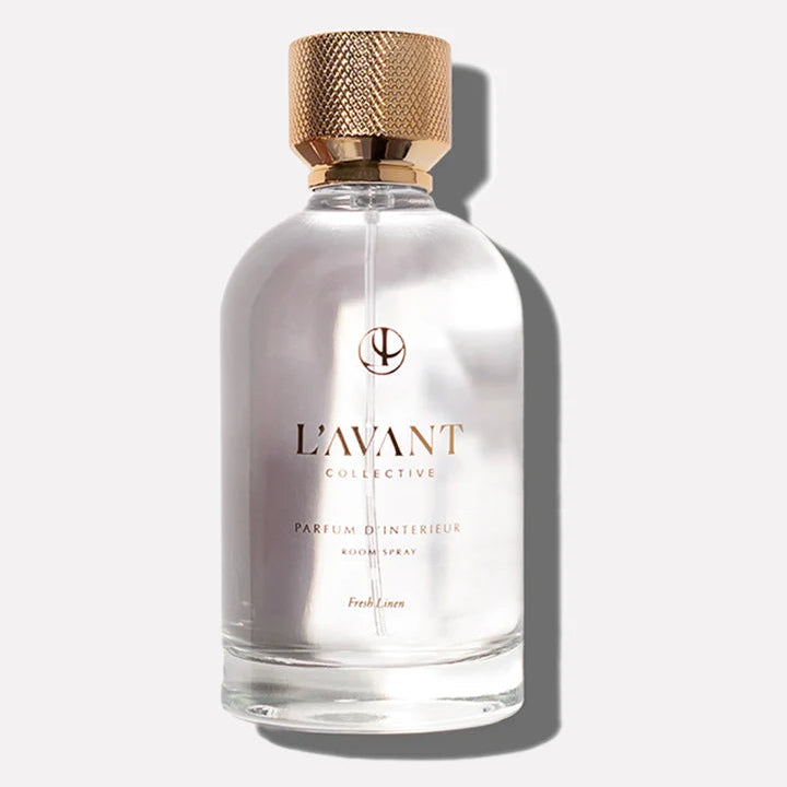 L’AVANT Collective Fresh Linen Parfum d’Intérieur Room Spray in a clear glass bottle with an elegant textured gold cap.