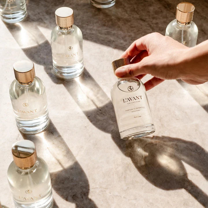L’AVANT Collective Fresh Linen Room Spray bottles styled in warm natural sunlight for an elegant luxury home fragrance display.