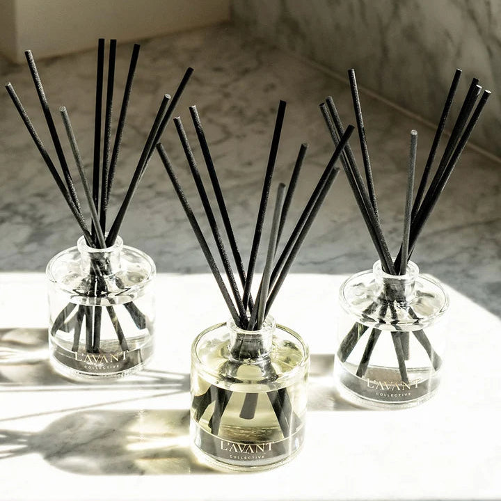 Three L’AVANT Collective luxury reed diffusers with clear glass vessels and black reeds displayed together in natural light.