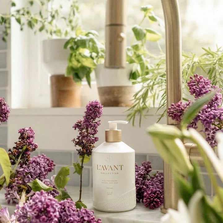 L’AVANT High Performing Dish Soap displayed beside a kitchen sink surrounded by fresh purple lilacs