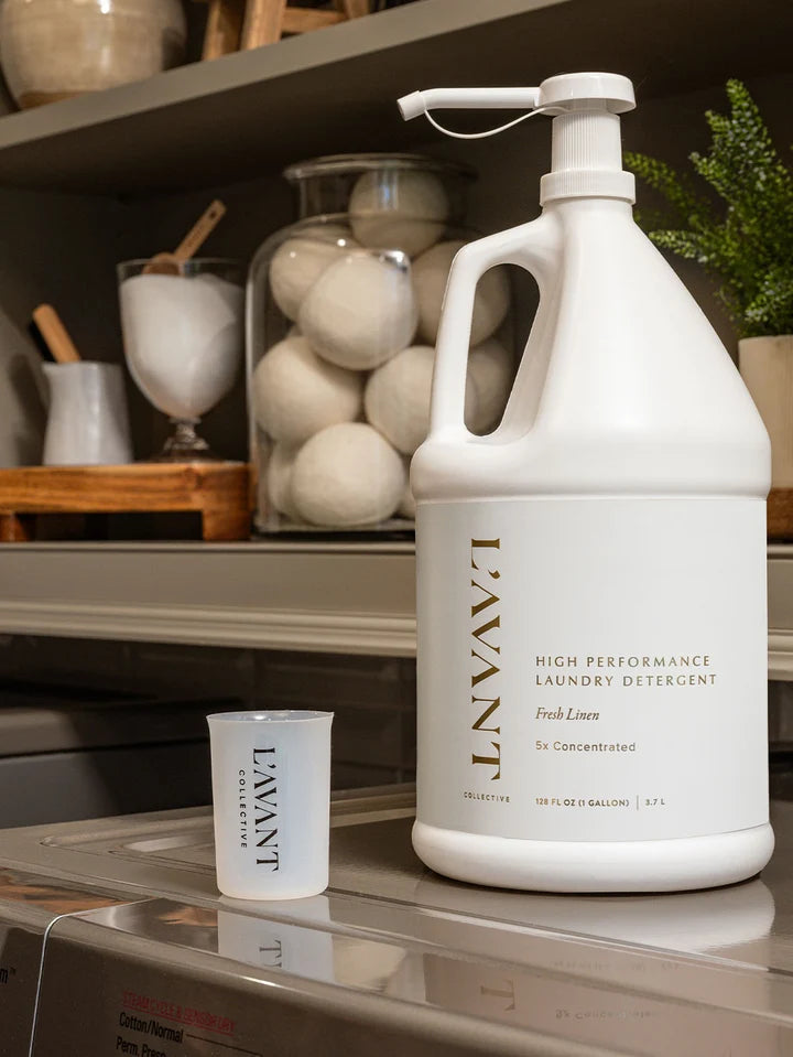 L’AVANT Collective Fresh Linen gallon laundry detergent with measuring cup in laundry room