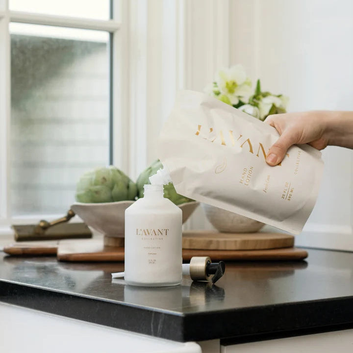 L’AVANT Collective Fresh Linen Hand Lotion refill pouch being poured into a reusable hand lotion bottle