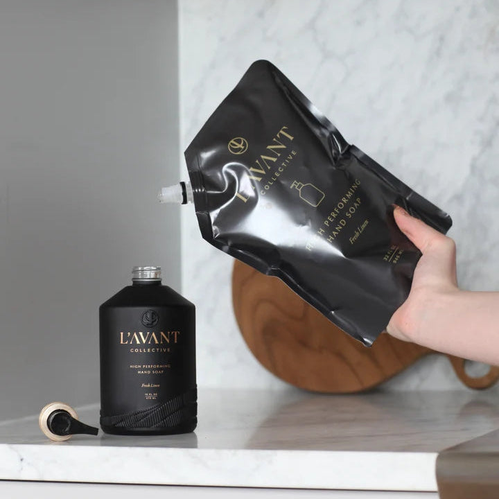 L’AVANT Collective Fresh Linen High Performing Hand Soap refill pouch being used to refill the black hand soap bottle
