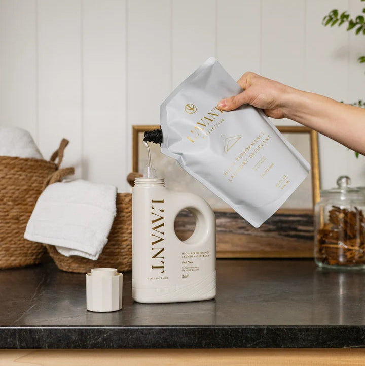 L’AVANT Collective Fresh Linen laundry detergent refill pouch being poured into detergent bottle